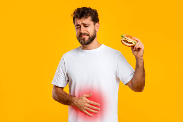 istock guy holding cheeseburger touching stomach on yellow studio background 2166933841