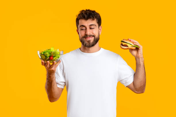 istock Smiling Caucasian Man Holding Cheeseburger And Healthy Vegetable Salad, Studio 2166933846