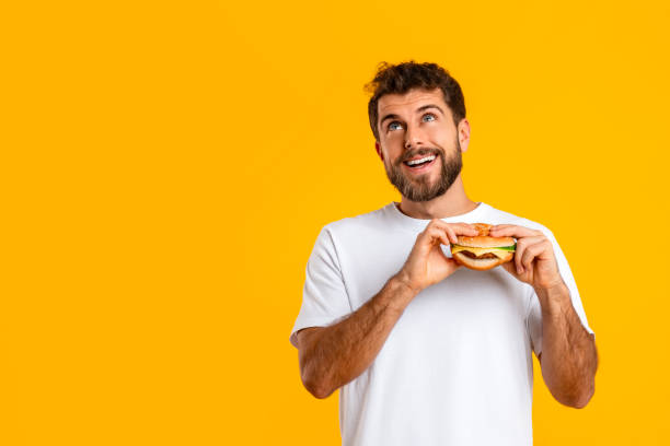 istock Hungry guy savoring takeaway cheeseburger near copyspace on yellow background 2166933848