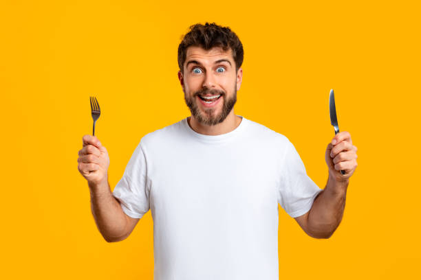 istock Hungry millennial man holds a knife and fork, yellow backdrop 2166933855