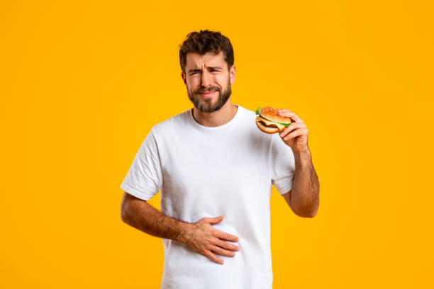 man experiences stomach discomfort after consuming burger on yellow background