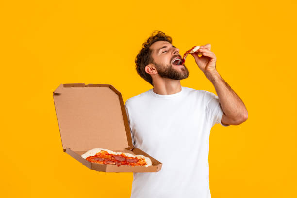 istock man holding delivery box and enjoying slice of pizza, studio 2166933889