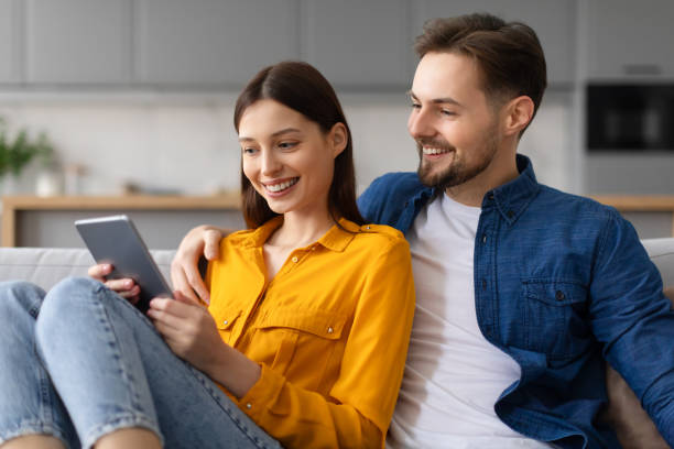 istock Couple smiling at tablet screen, resting on couch at home 2166934776