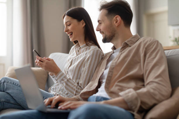 istock Joyful young couple using laptop and smartphone on couch 2166934800