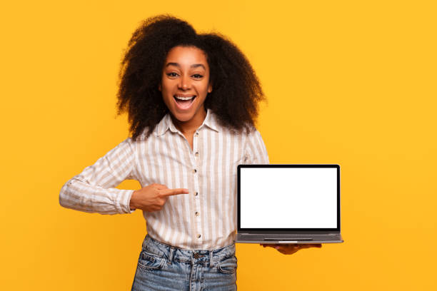 istock Happy black lady showing laptop with blank screen, yellow backdrop 2166934872