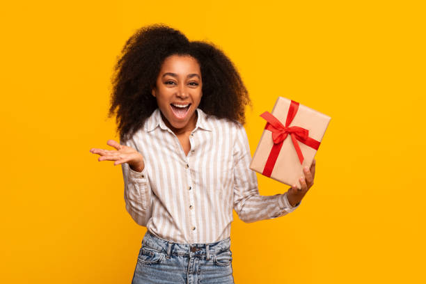 istock Excited woman holding a gift box on yellow background 2166934902