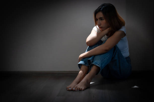 A young woman sits alone in a dimly lit room, reflecting on her struggles with depression, anxiety, and loneliness. She appears deep in thought, conveying a sense of sadness and despair.