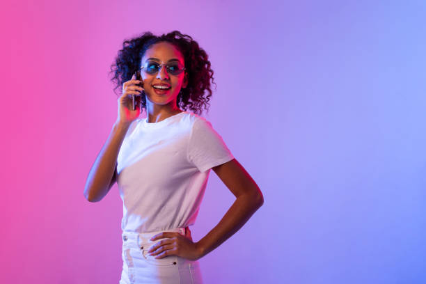 istock Stylish black woman talking on phone with neon lights backdrop 2166947639