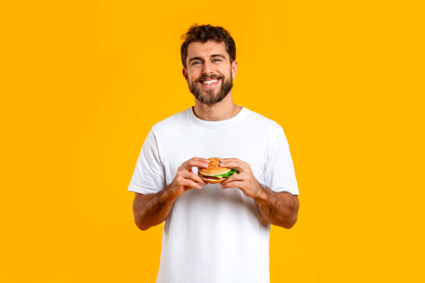 istock Happy European man posing holding a cheeseburger on yellow backdrop 2166948545