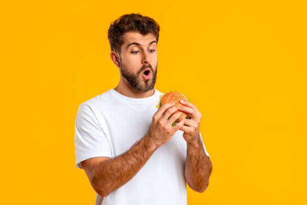istock Excited Guy Holding Looking At Takeaway Burger On Yellow Background 2166948547