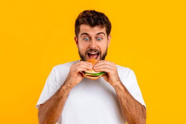 istock Excited hungry Caucasian man biting delicious cheeseburger against yellow backdrop 2166948551