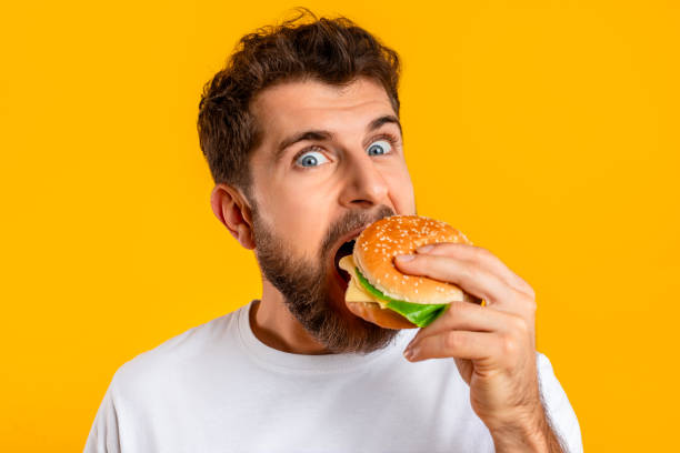 istock funny guy satisfying food cravings with cheeseburger on yellow background 2166948554