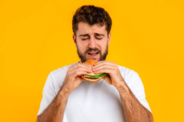 istock Unhappy bearded young man eats burger over yellow backdrop 2166948560