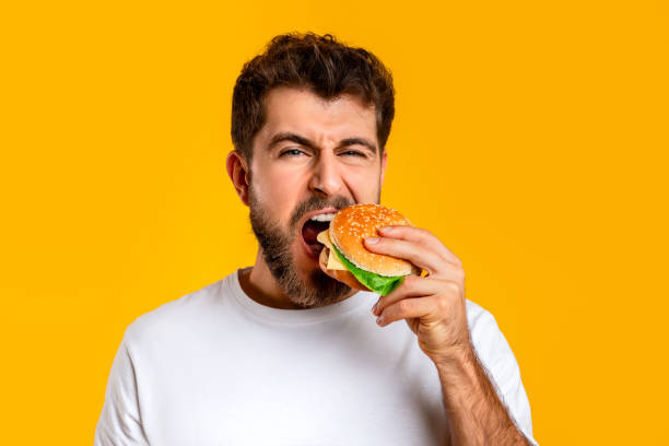 istock Hungry Guy Taking Bite Of Burger On Yellow Backdrop, Closeup 2166948572
