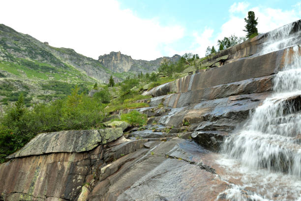 istock Steep stone steps from which a rapid waterfall cascades down in a coniferous forest under a summer cloudy sky. 2166952917