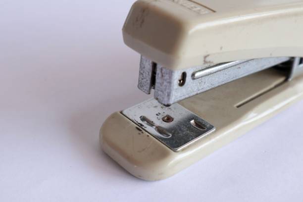 A small mint-colored office stapler is depicted on a dark gray background. The stapler is positioned at a slight angle, its top part is open. Staples for the stapler are not visible.