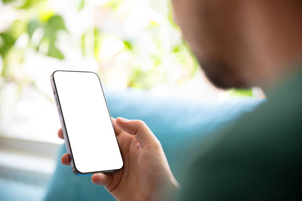 istock Person holding a smartphone with a blank screen, relaxing on a sofa in a bright, green environment. Perfect image for presenting mobile apps, user interfaces, or design templates. 2166973216