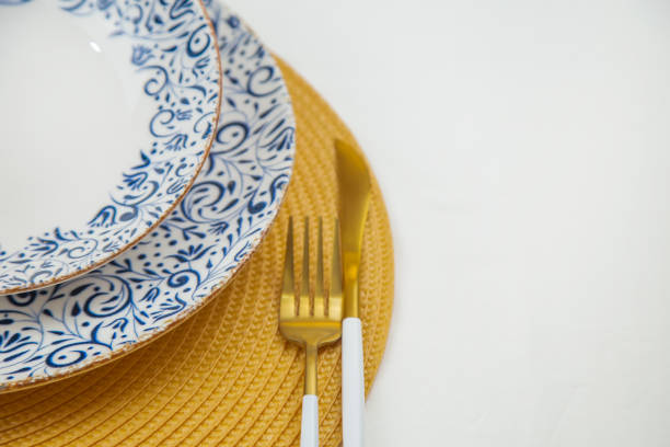 istock A white soup plate with a blue pattern on the edges stands on a blue-and-white patterned serving plate in close-up on a yellow straw napkin, next to cutlery are a knife and fork, on a white background. 2166978022