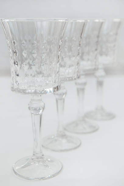 istock Crystal wine glasses on a long stem, with expanded edges and a faceted pattern stand in a row on a white background, the first one is in focus on the sides, the second ones stand behind it in focus. 2166978403