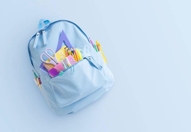 Backpack with colorful school supplies on light blue background with copy space