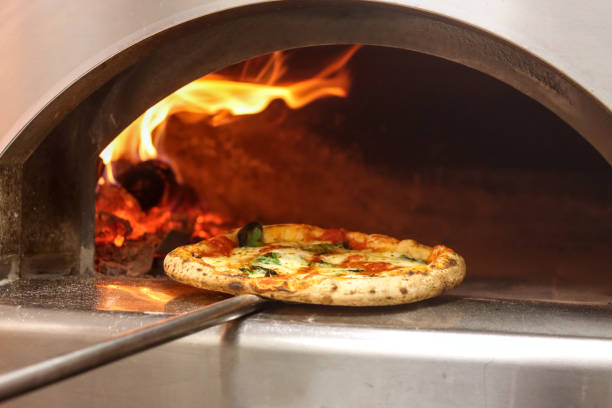 Wood-fired pizza being cooked in a traditional oven with flames visible