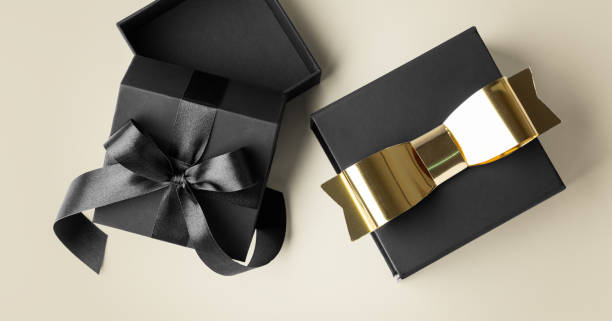 istock Black gift box open and present with gold bow on light gold background 2166988759