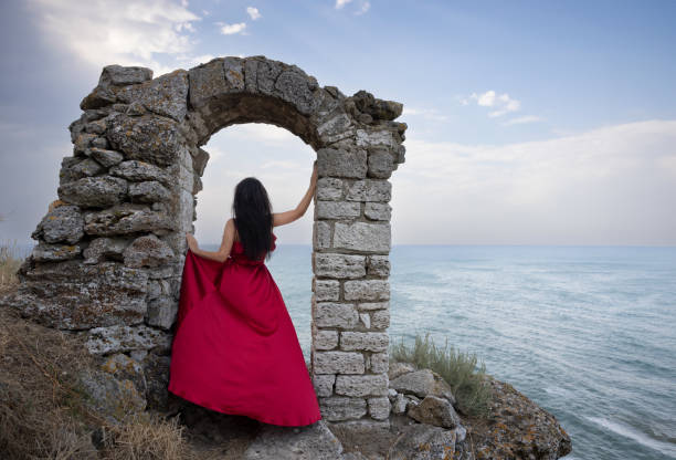 Young romantic woman wearing a vaporous red dress posing on the spectacular arch in Cape Kaliakra, Bulgaria.