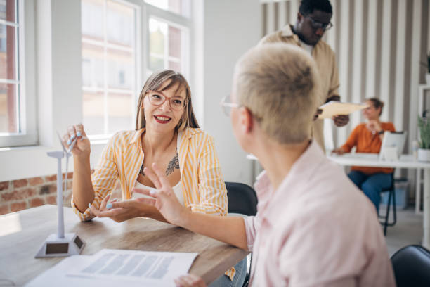 istock Two women conversing at a desk with wind turbine models. 2166999334