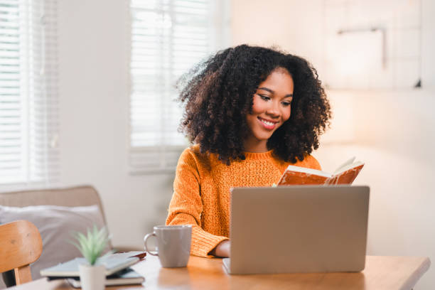istock Smiling African American woman reading a notebook while working at home, sitting at a desk with a laptop and a coffee mug. 2167005997