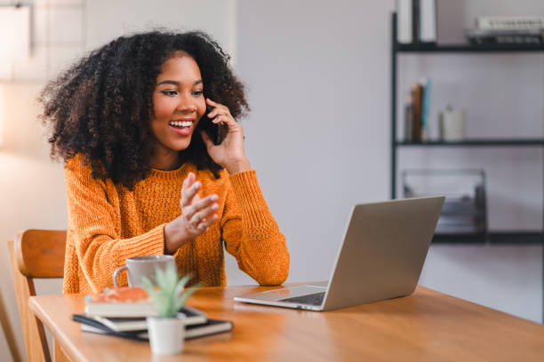 istock African American woman having phone conversation while working at desk with laptop. 2167006012