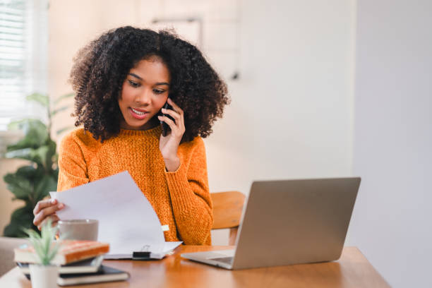 istock African American woman multitasking at desk, speaking on the phone while reviewing documents, with a laptop at home. 2167006042