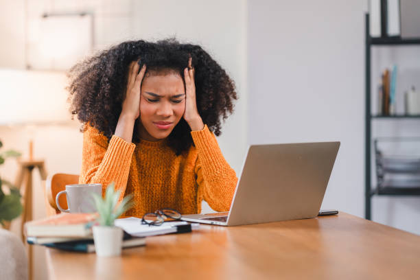 istock African American woman feeling stressed and holding her head in frustration while working on a laptop at home. 2167006114