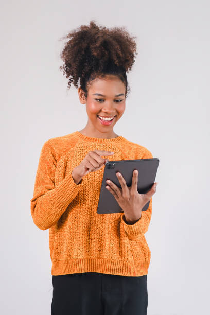 istock Happy woman in an orange sweater smiling while using tablet, engaging with content on white background. 2167007655