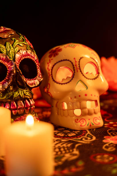 istock Vertical composition featuring two skulls on a Day of the Dead tablecloth: one decorated with metallic flowers, the other hollow with a lit candle 2167010855