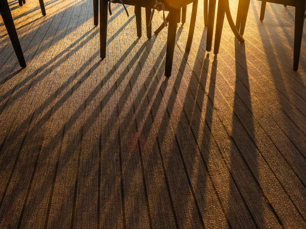 Long evening shadows of a small table and chairs in low sunlight on carpeted upper deck of a cruise ship under way in southeastern Alaska