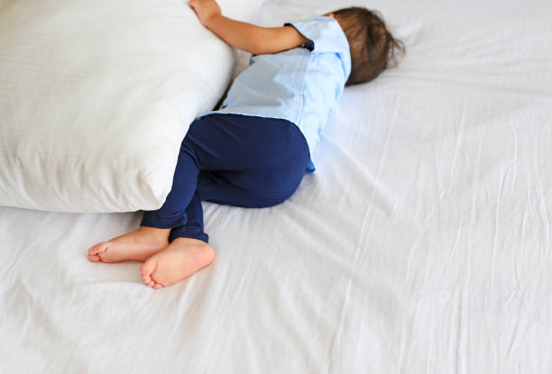 Baby boy sleeping on bed with hugging a pillow. Rear view.