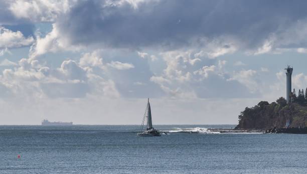 istock Sailboat on the ocean with a lighthouse on the coastline under a cloudy sky 2167020848