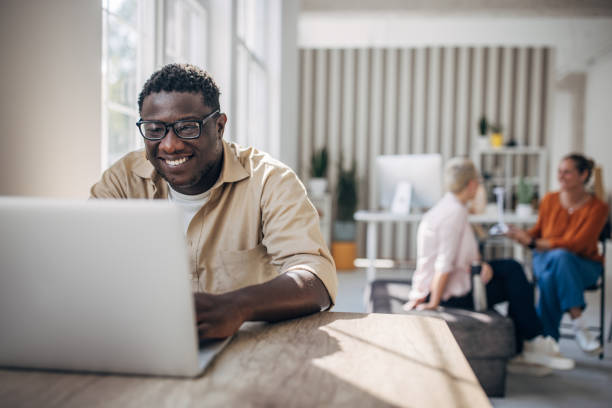 istock Man smiling and working on laptop in sunlit office 2167021050