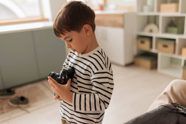 A little Caucasian boy playing with a film camera in the living room of the apartment he lives in