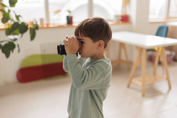 A little Caucasian boy playing with a film camera in the living room of the apartment he lives in