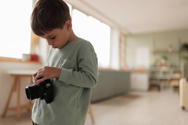 A little Caucasian boy playing with a film camera in the living room of the apartment he lives in