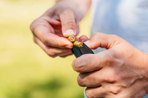 Mid-adult man inserting bullets into his handgun, loading the weapon in preparation for shooting practice. Close-up.
