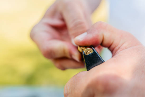 Mid-adult man inserting bullets into his handgun, loading the weapon in preparation for shooting practice. Close-up.