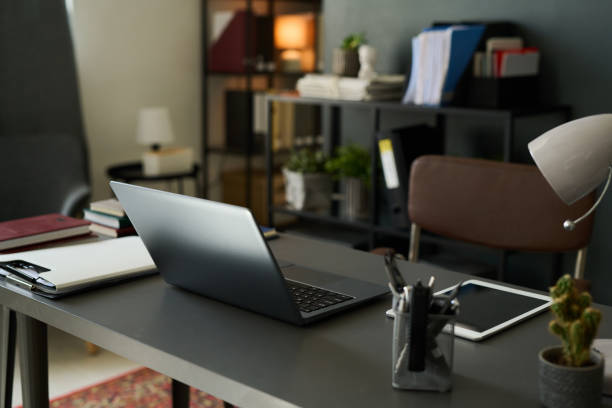 Modern home office setting with laptop on desk surrounded by books, notebooks, and shelves providing an organized and efficient workspace