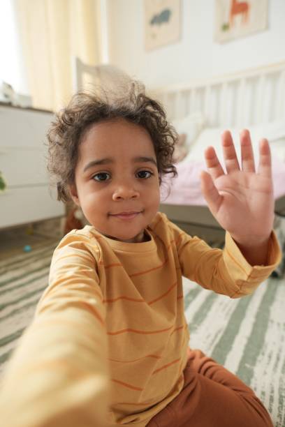 istock Waving Toddler in Cozy Bedroom with Sunlight 2167025983