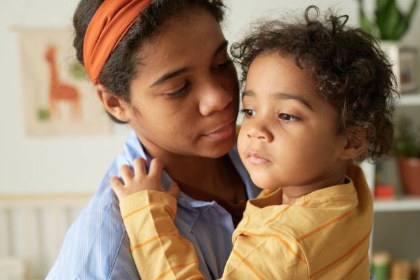Embracing Mother and Child with Tenderness Mother embracing her child, holding lovingly while standing in cozy room setting with animal posters on wall, capturing genuine moment of maternal care and connection young hot stock pictures, royalty-free photos & images