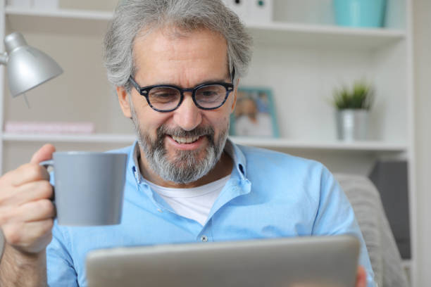 istock Smiling Elderly Man Holding a Gray Coffee Cup While Using a Tablet in a Cozy Home Environment 2167029758