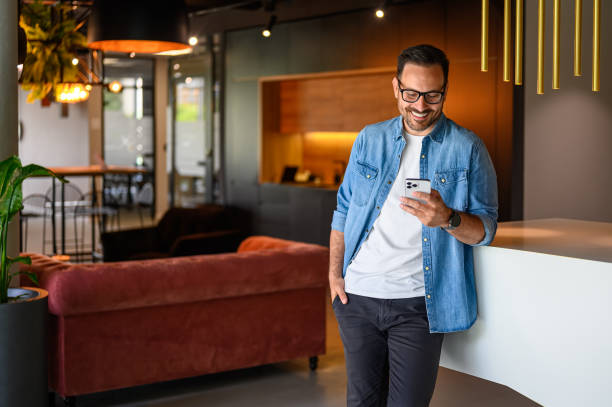 istock Smiling male freelancer with hand in pocket texting over mobile phone while standing by table in office 2167029816