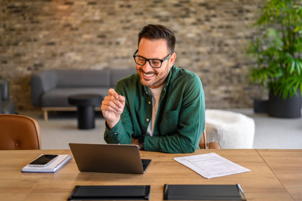 istock Smiling male programmer in eyeglasses looking at computer while designing website at desk in office 2167029827