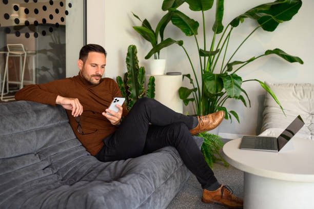 istock Serious young man holding glasses and reading e-mails over smart phone while sitting on sofa in office 2167029892